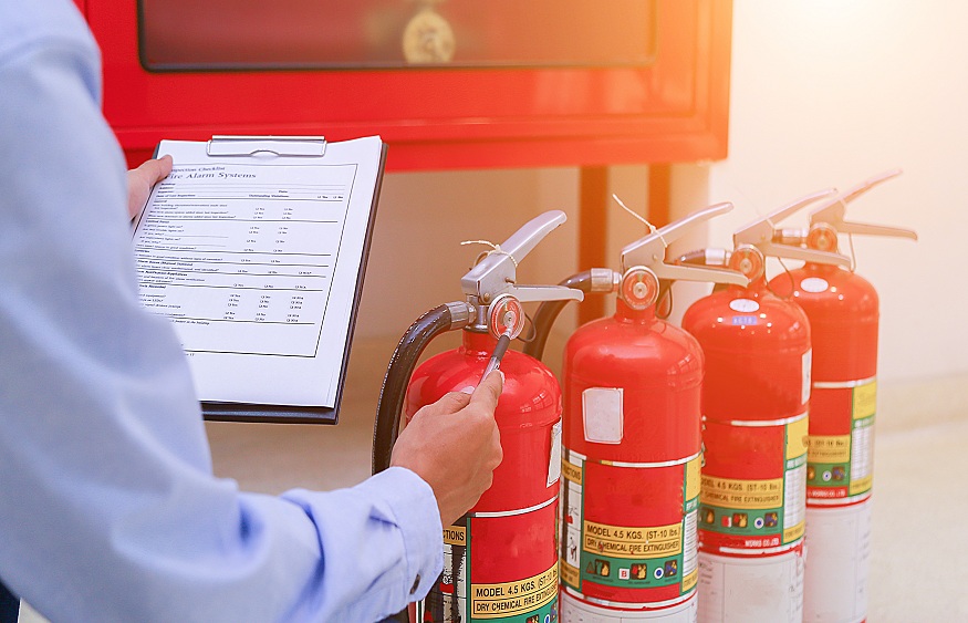 Man holding checklist board next to row of fire extinguishers